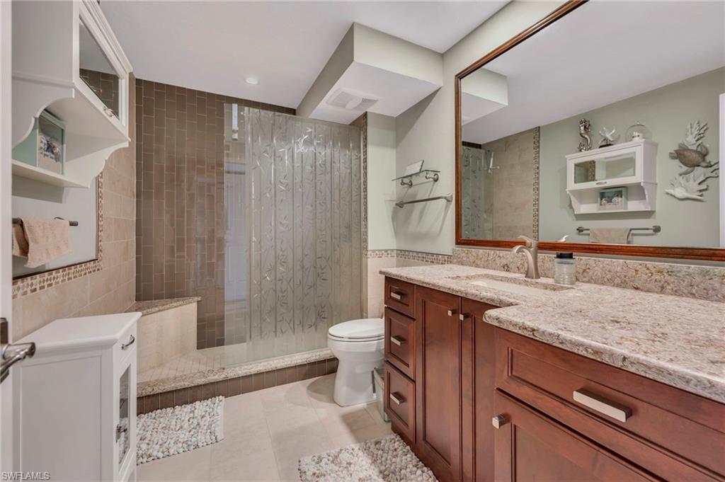 Bathroom with a glass-enclosed tiled shower and wood vanity with a stone countertop.