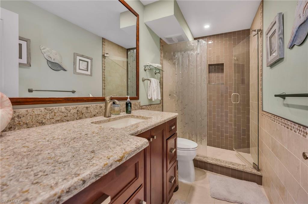 Bathroom with a granite vanity and glass-enclosed tiled shower.