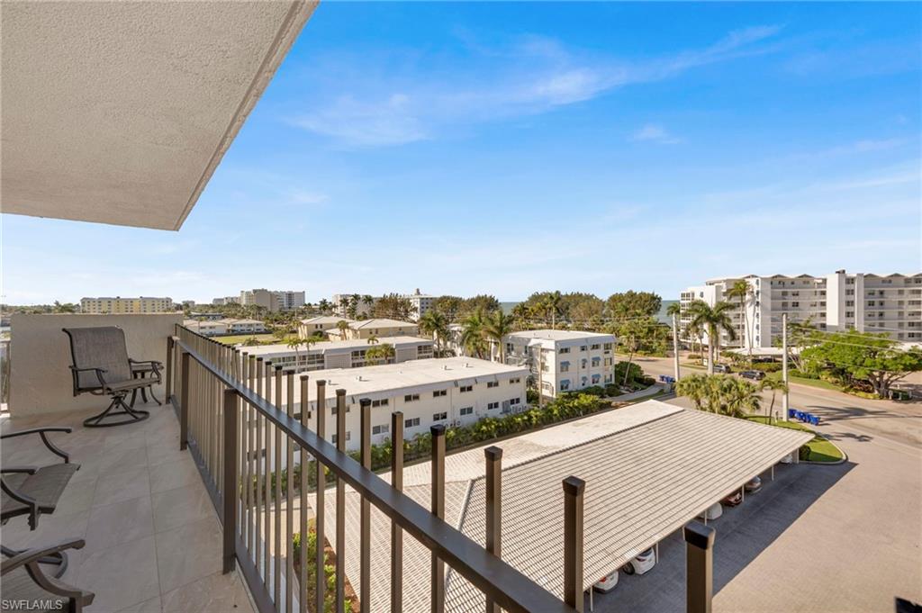 Condominium balcony overlooking palm-lined buildings and a parking area, with a glimpse of water.