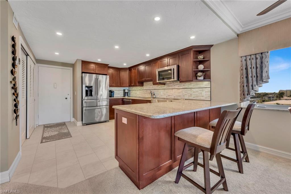 Condo kitchen with a granite island, wood cabinetry, stainless steel appliances, and a window overlooking nearby buildings.