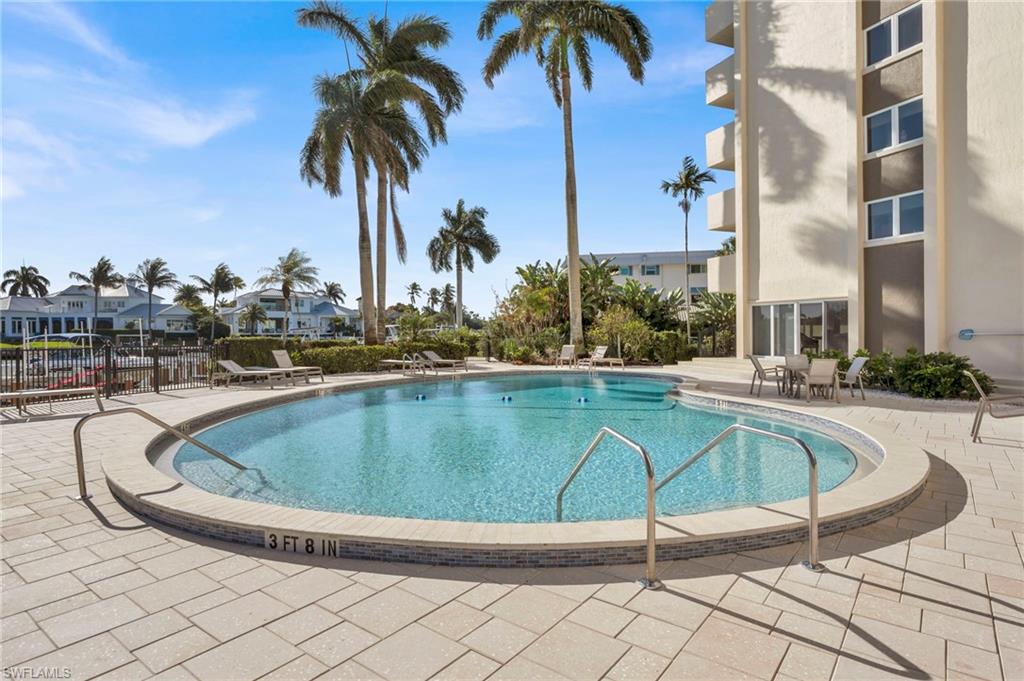 Outdoor condominium pool with curved edge, metal handrails, palm trees, and poolside lounge chairs.