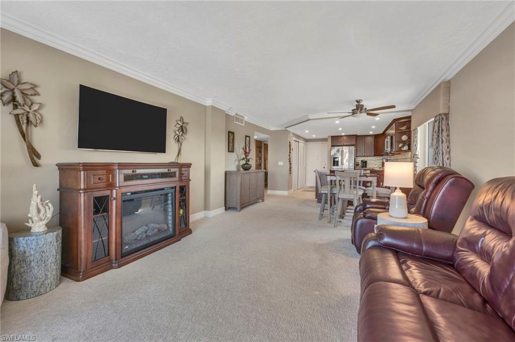 Furnished living room with a wood fireplace cabinet, brown leather seating, and an open kitchen and dining area.
