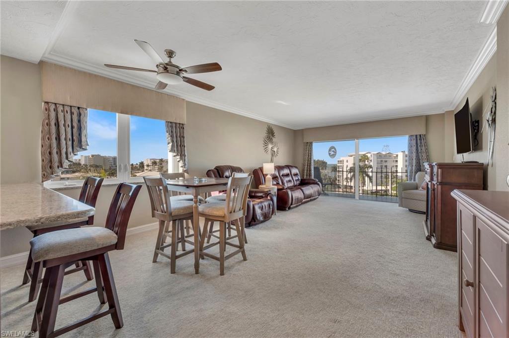 Living and dining room with leather seating and balcony doors overlooking neighboring buildings and palm trees.