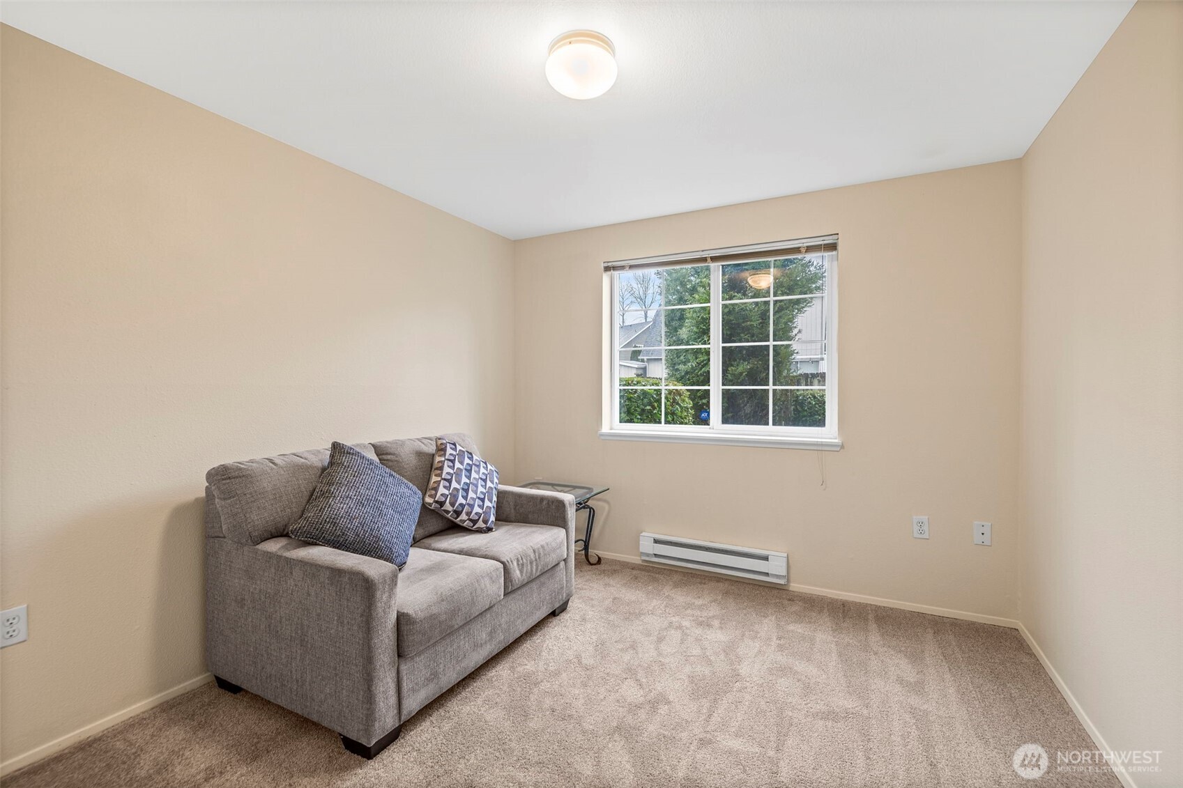 Furnished room with a gray loveseat, patterned cushions, and a window overlooking greenery.