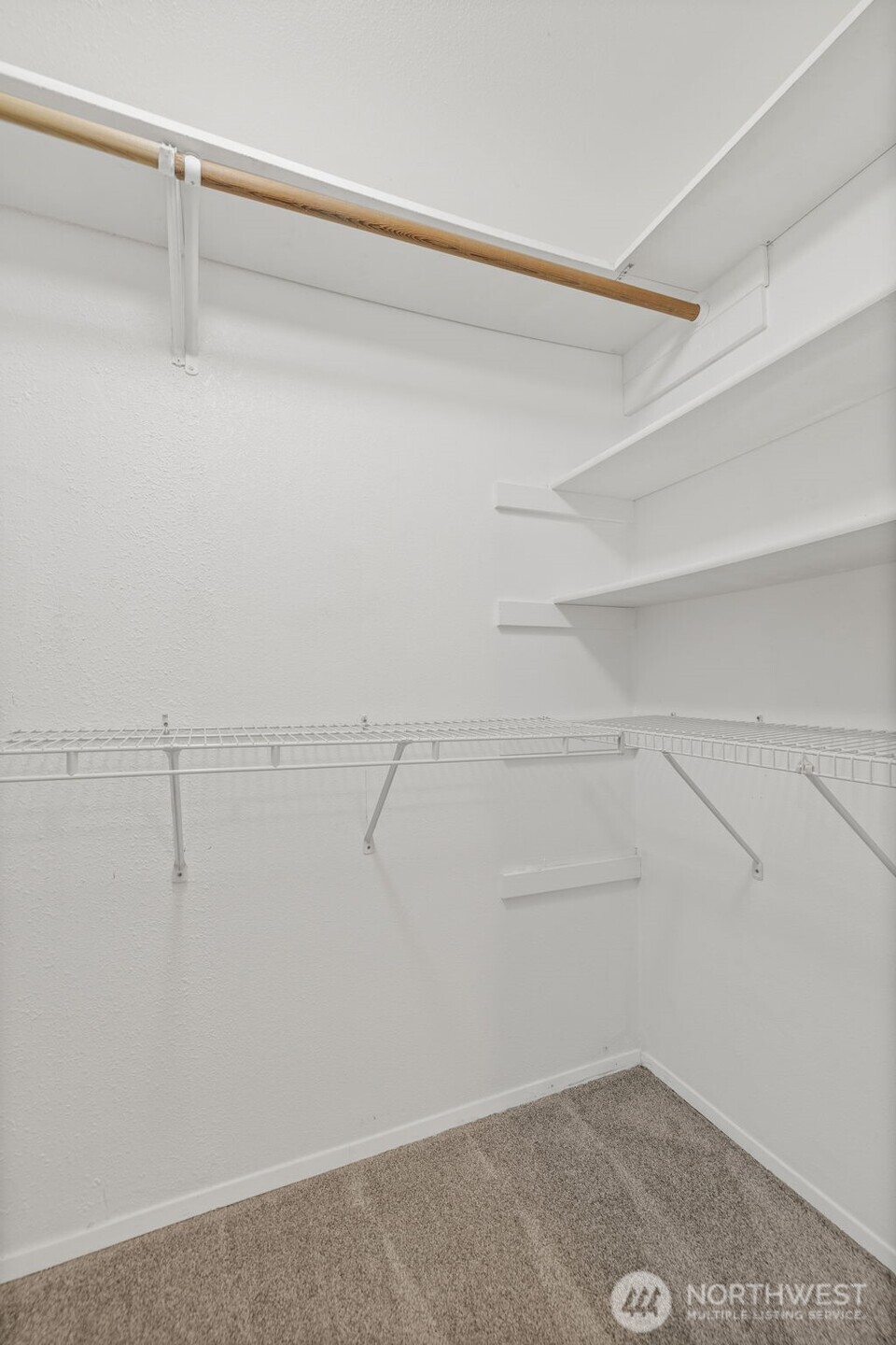 Empty walk-in closet with wire shelving, a wooden hanging rod, and beige carpet.