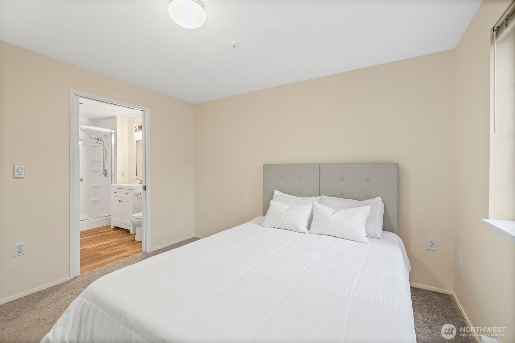 Bedroom with a white bed and gray tufted headboard, opening to an adjoining bathroom.