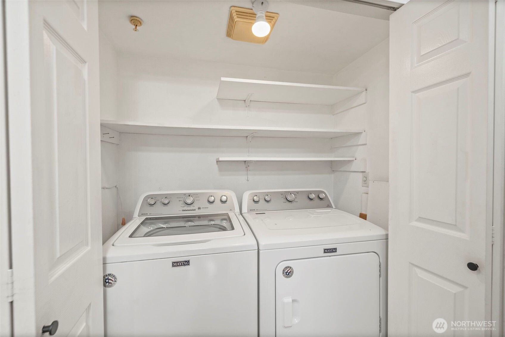 Laundry room with Maytag washer and dryer beneath wall-mounted shelves.