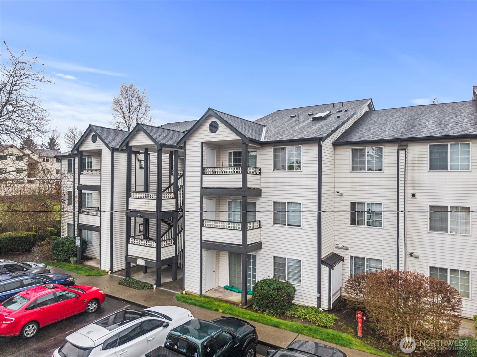 Condominium building with stacked balconies and parked cars in front.