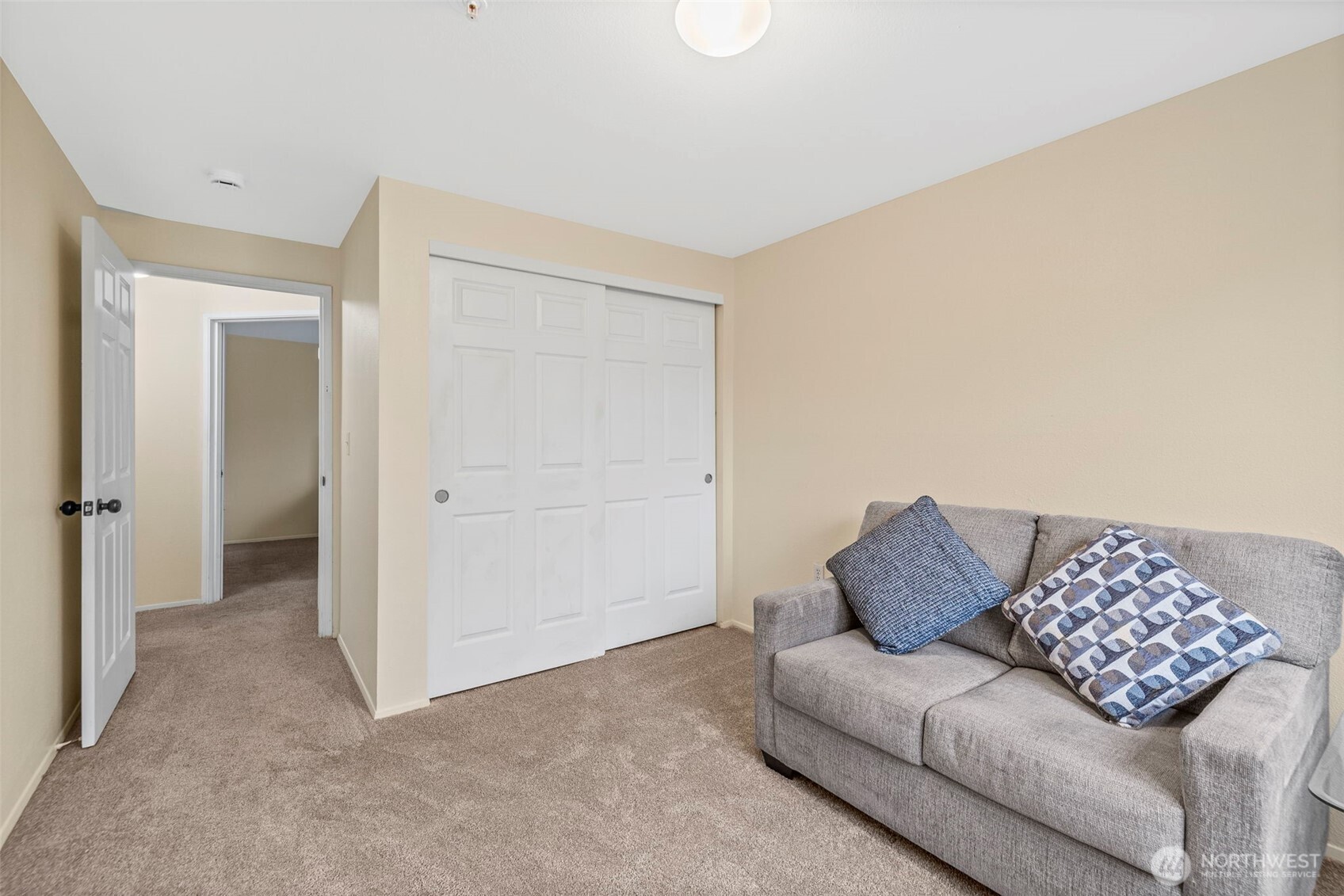 Carpeted room with white sliding closet doors and a gray sofa with patterned pillows.