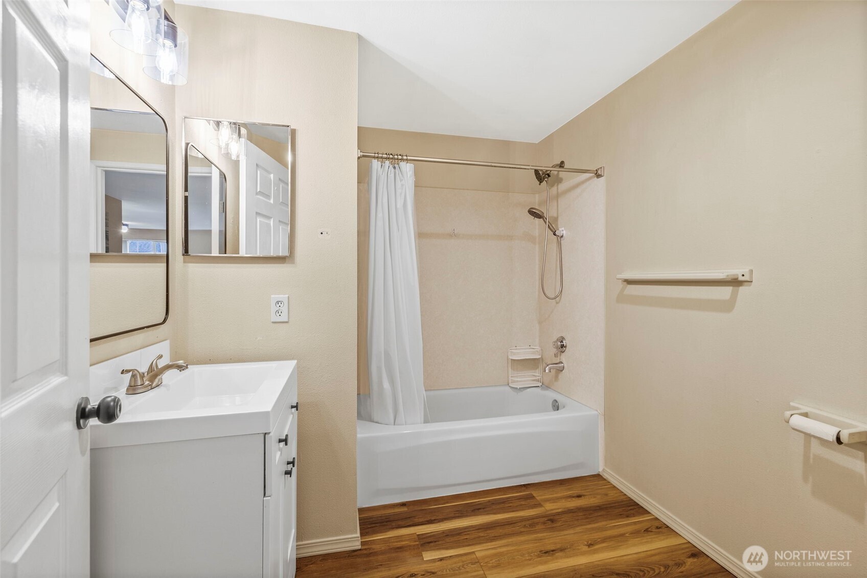 Bathroom with a white vanity, bathtub and shower, and wood-look flooring.