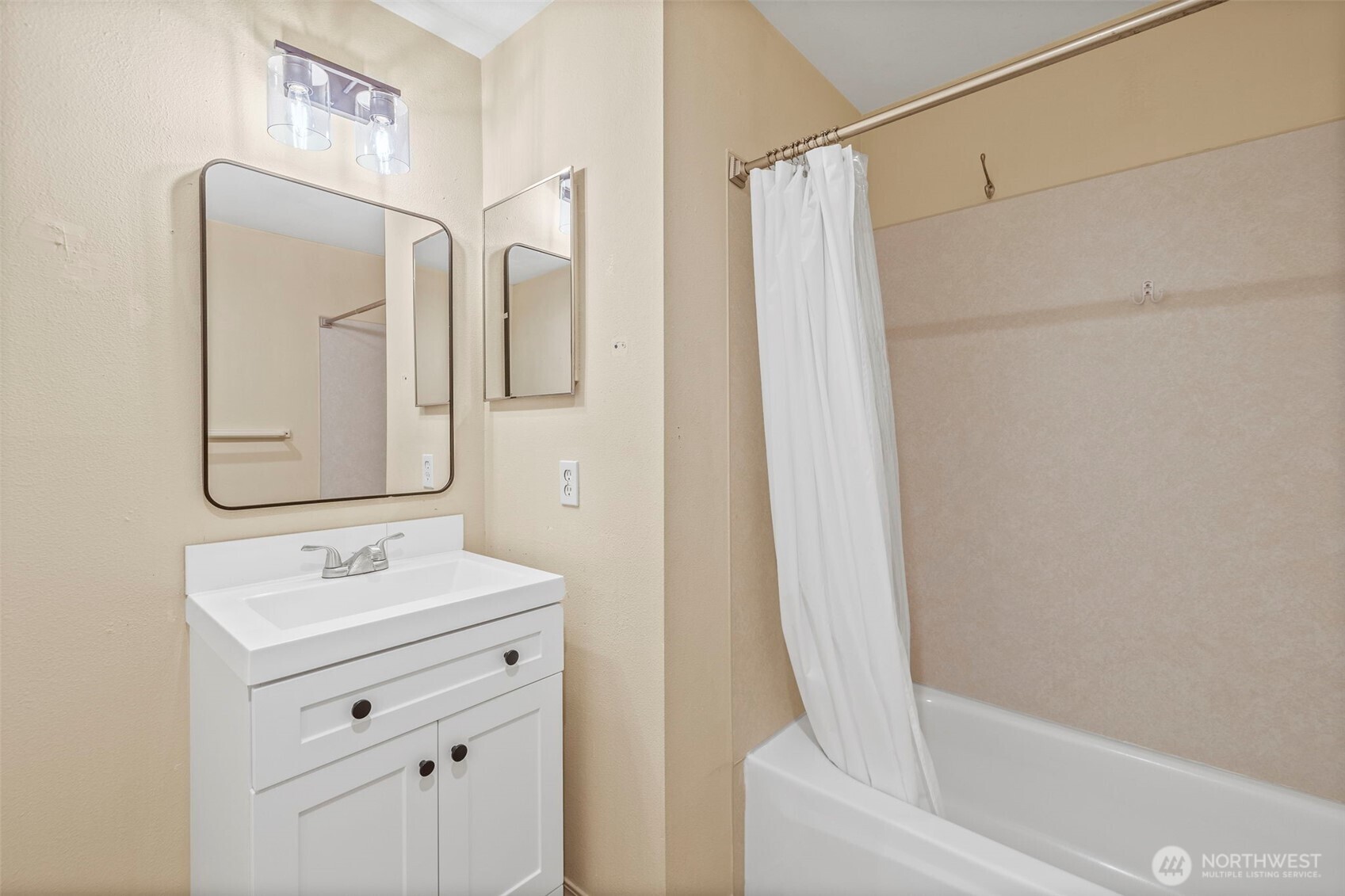 Bathroom with a white vanity, large mirror, and bathtub behind a white shower curtain.