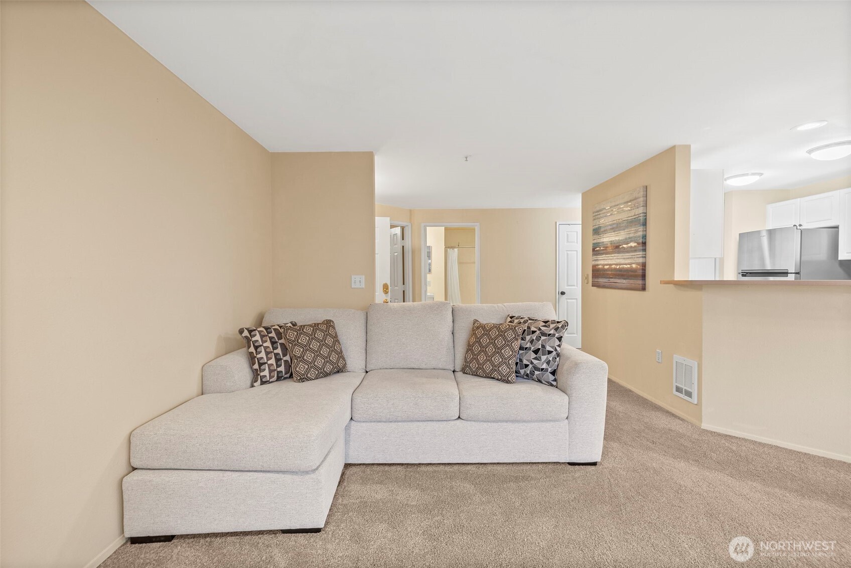 Living room with a light gray sectional sofa, patterned pillows, and a pass-through to the kitchen.