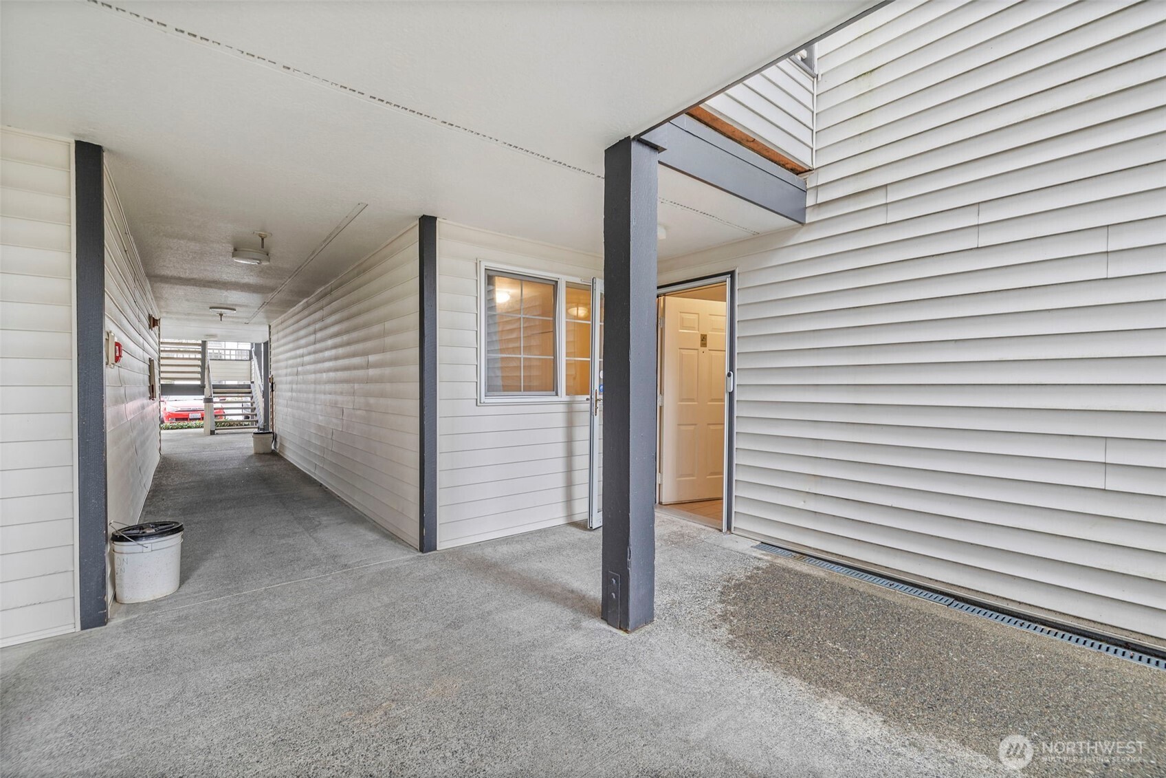 Condo entrance along a covered walkway, with white siding, dark posts, and stairs at the far end.