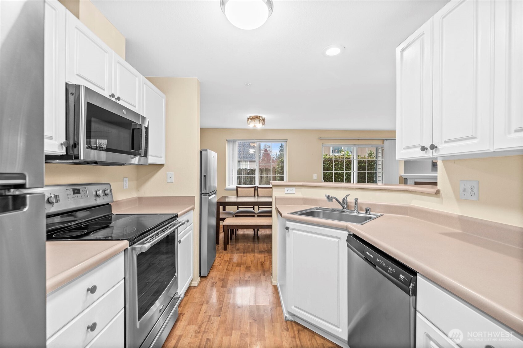 Condo kitchen with stainless steel appliances, white cabinets, and a breakfast bar opening to a dining area.