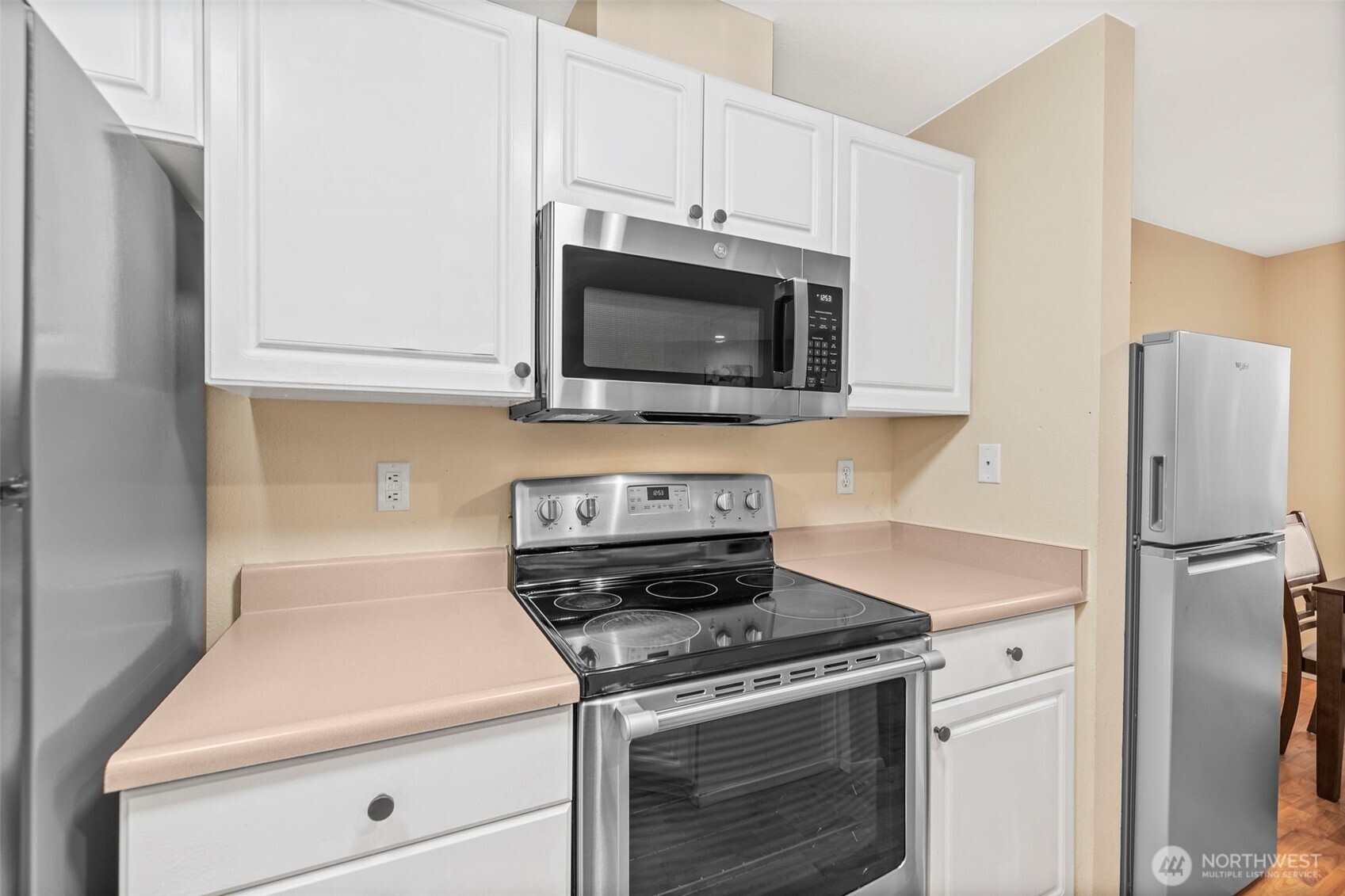 Kitchen with white cabinets, stainless steel appliances, and pale pink countertops.