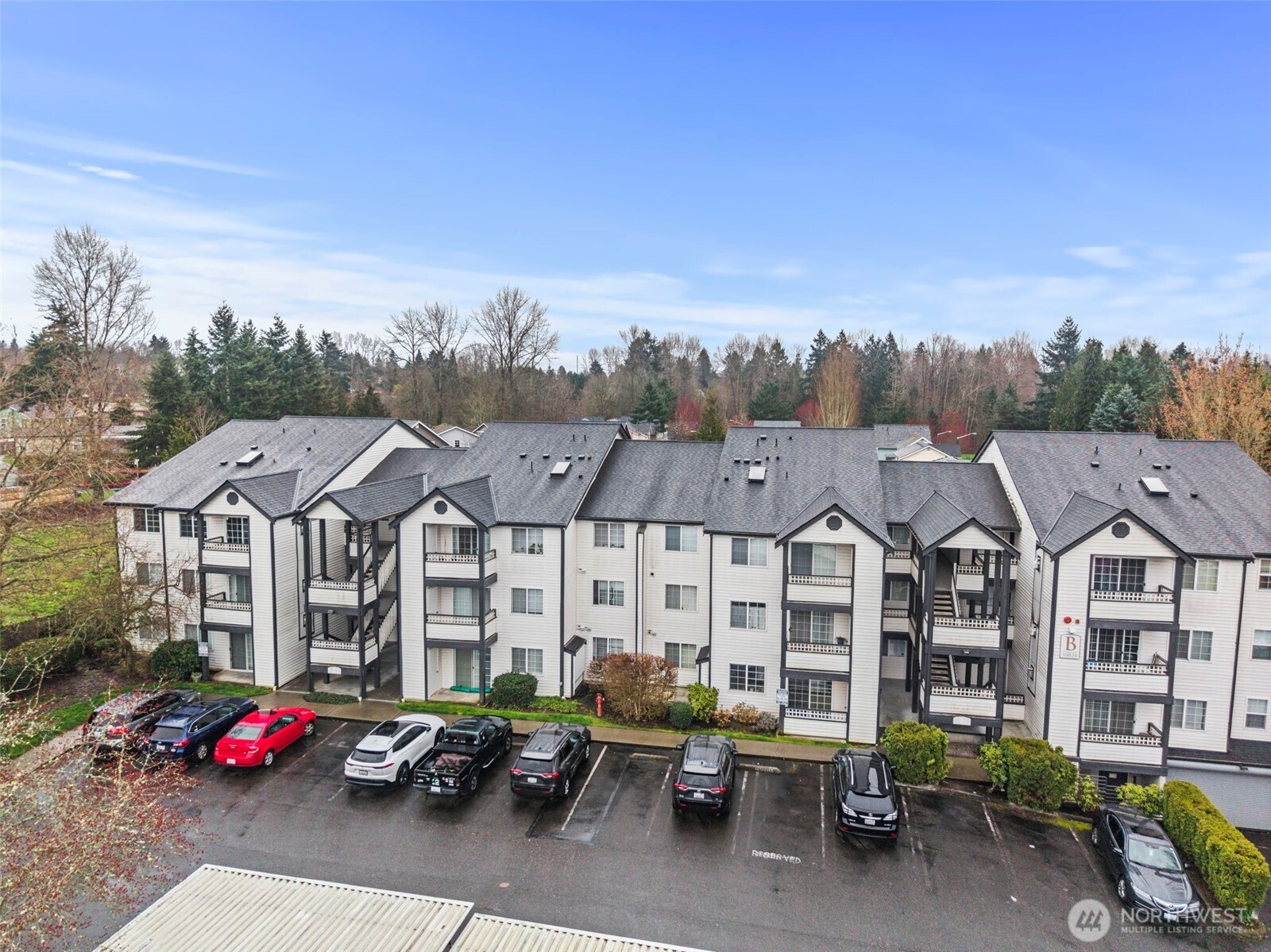 Elevated view of a white condominium complex with dark roofs, balconies, and a front parking lot.