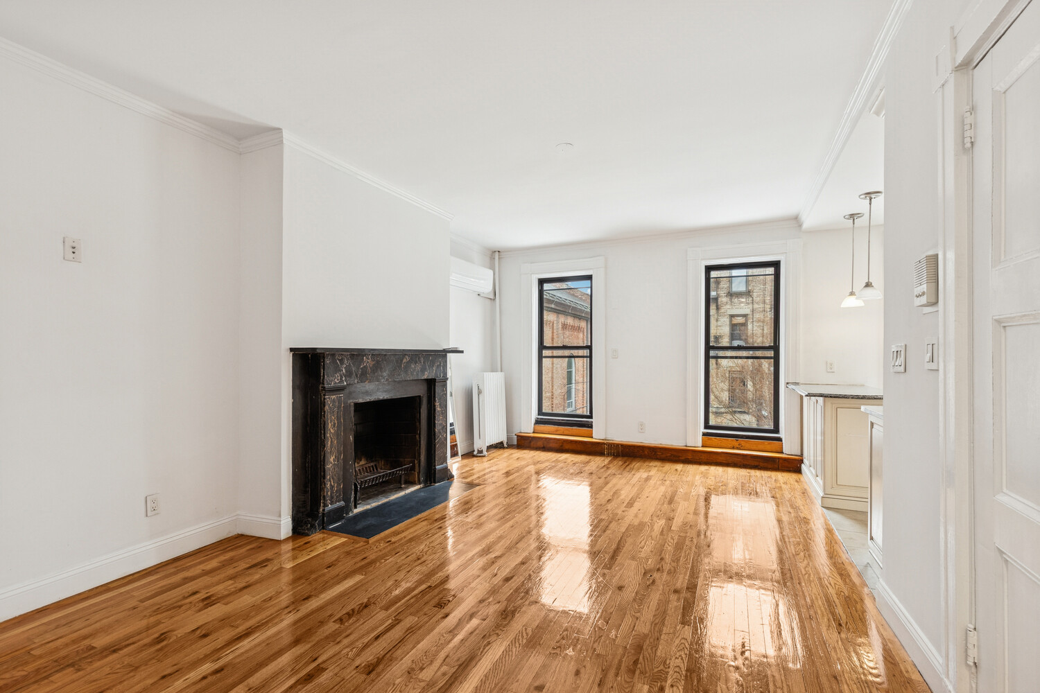 Living room with a dark fireplace, polished hardwood floors, and tall windows.