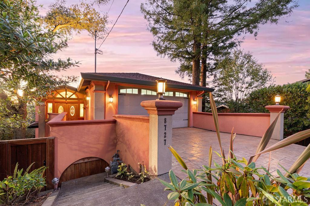 Stucco home with an arched entry, tiled driveway, and pink perimeter walls at dusk.
