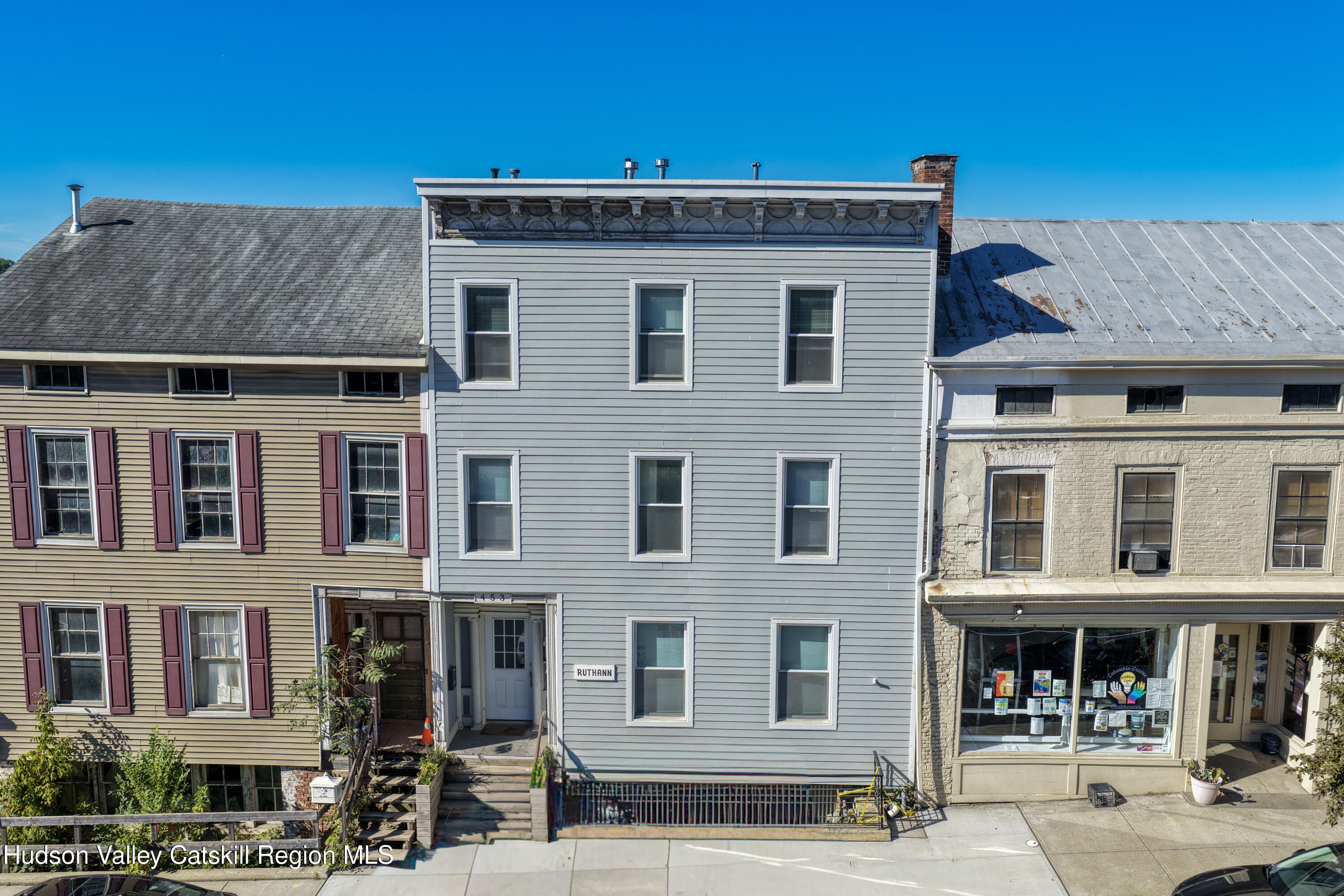 Three-story gray-sided building with white-trimmed windows, marked 453, between two neighboring storefronts.
