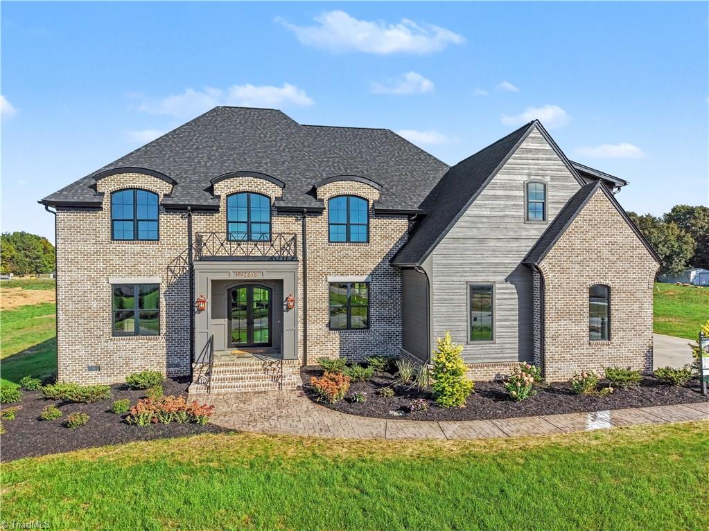 Two-story brick and gray-sided home with arched windows and a curved front walkway.