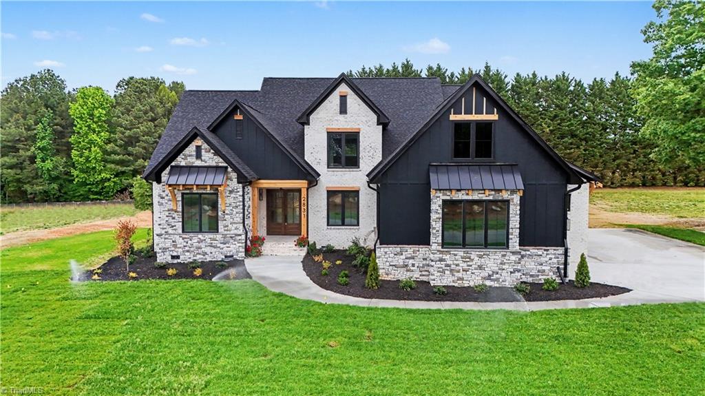 Two-story house with dark gables, stone walls, and a landscaped front lawn.