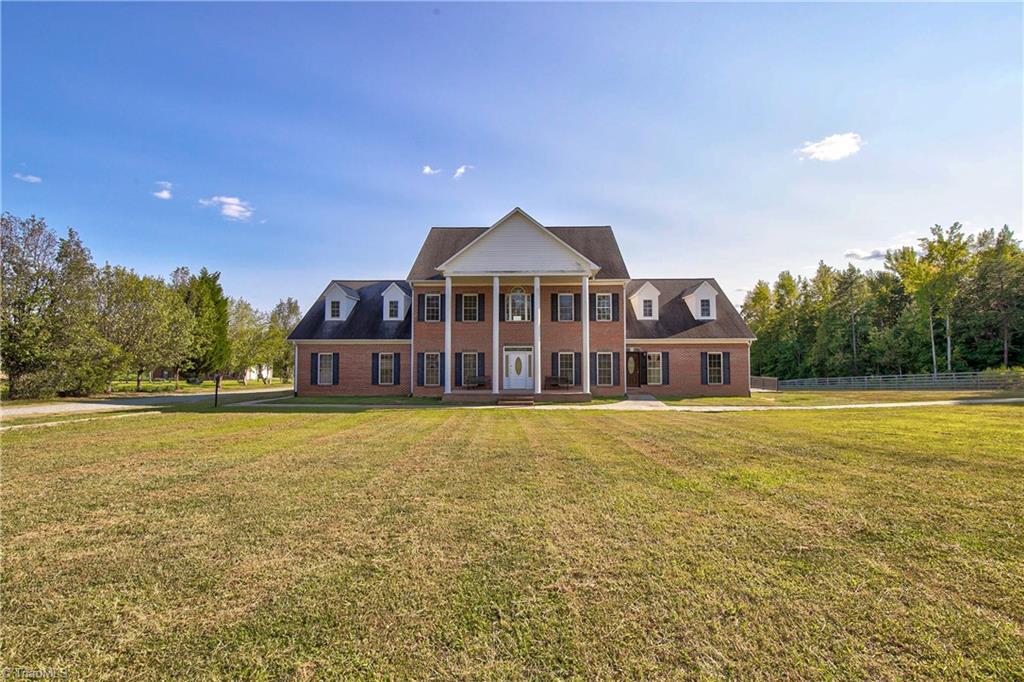 Two-story brick house with white columns and dormer windows, set beyond a broad lawn.