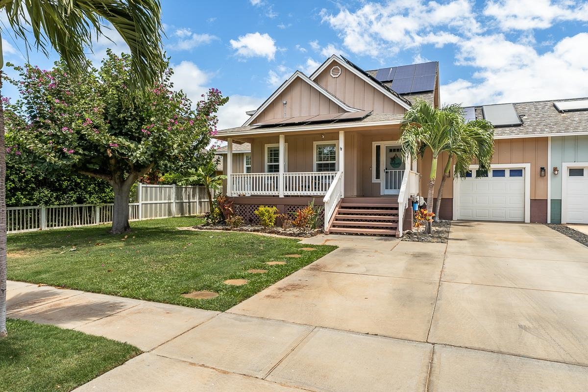Tan home with a covered porch, attached garage, solar panels, and tropical landscaping.