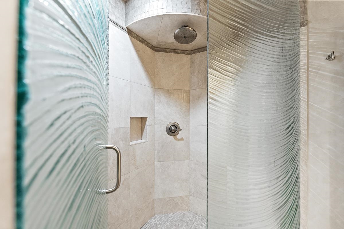 Walk-in shower with a rainfall showerhead, recessed niche, and textured glass doors.