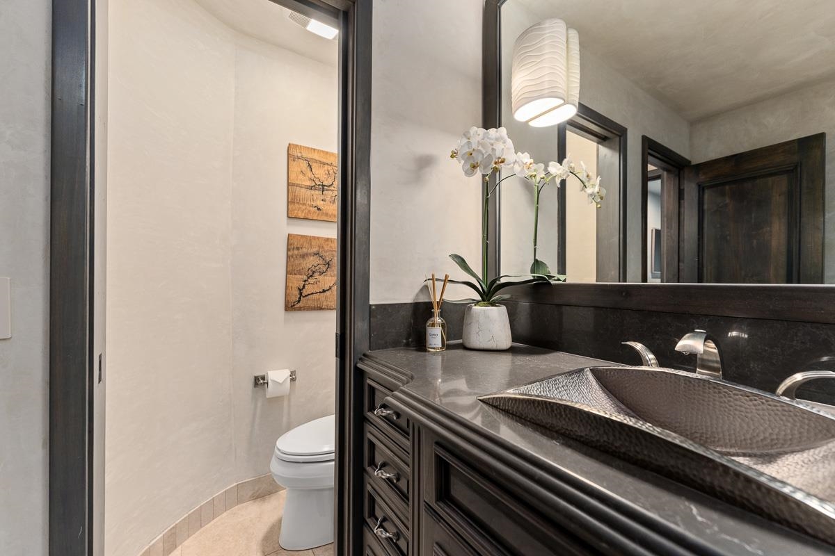 Bathroom with a dark wood vanity, hammered vessel sink, and orchid beside a separate toilet area.