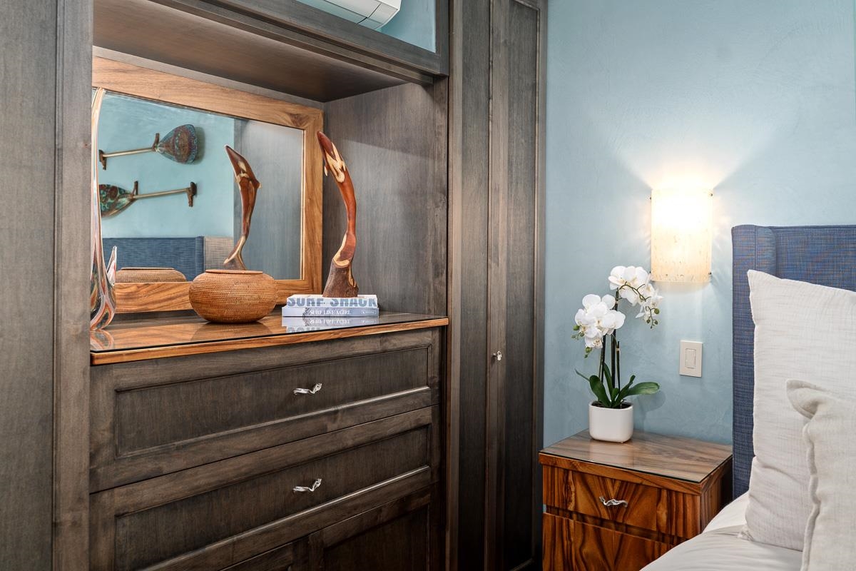 Bedroom with a dark wood dresser and mirror beside a wooden nightstand topped with a white orchid.
