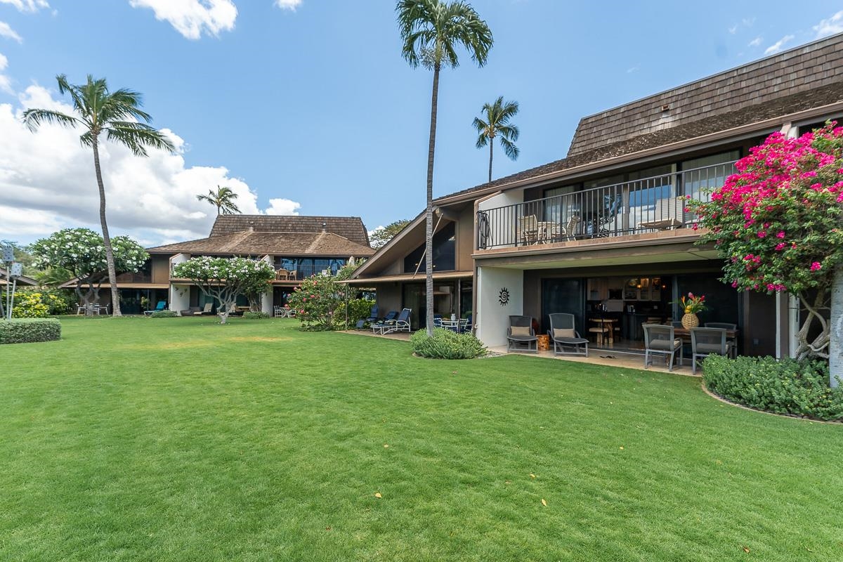 Two-story condominium with furnished lanais, a broad lawn, palm trees, and bright pink bougainvillea.