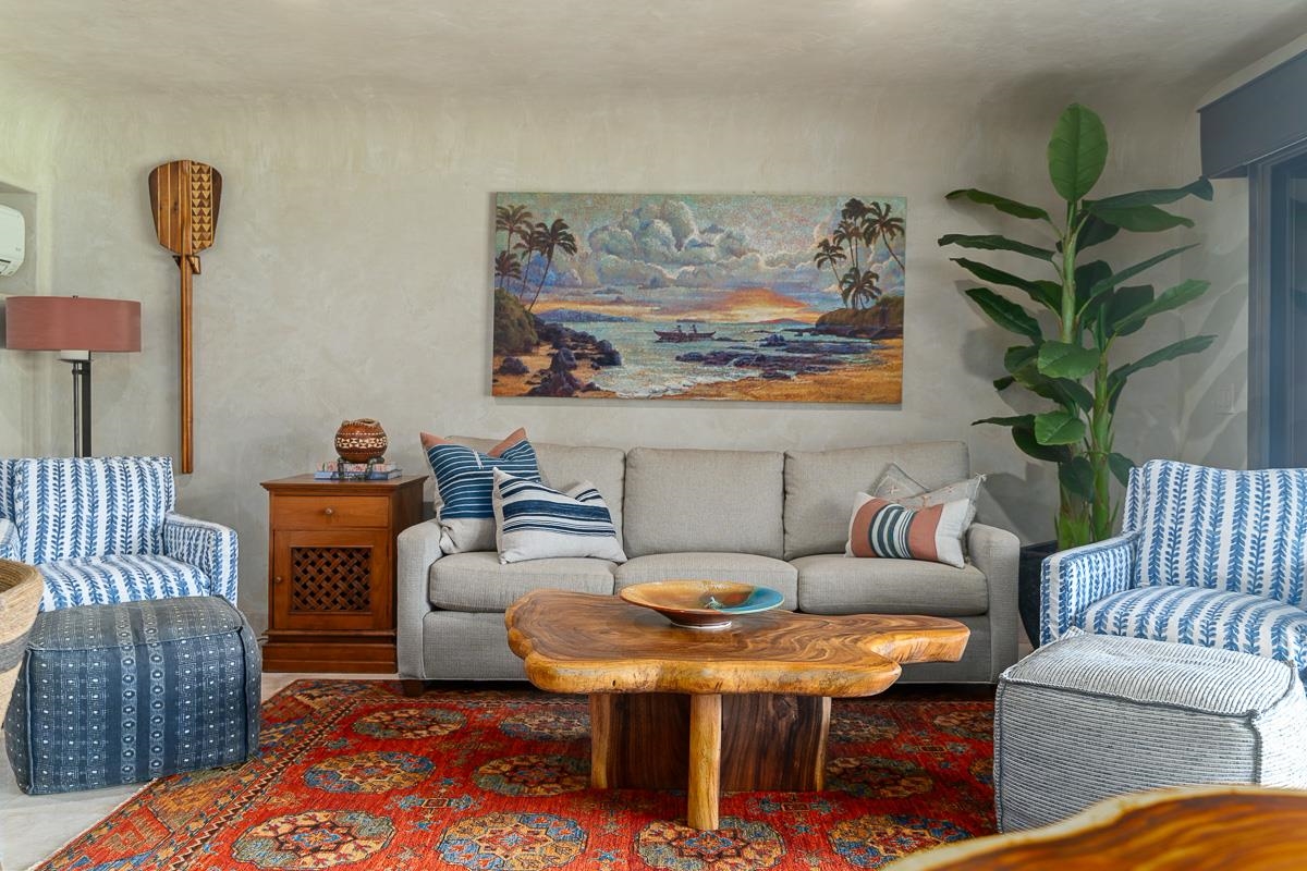 Living room with a beige sofa, patterned armchairs, carved wood coffee table, and colorful rug.