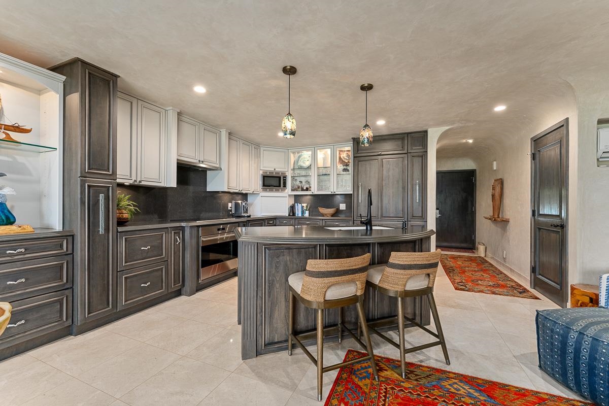 Kitchen with dark cabinetry, a curved breakfast island, and colorful pendant lights.