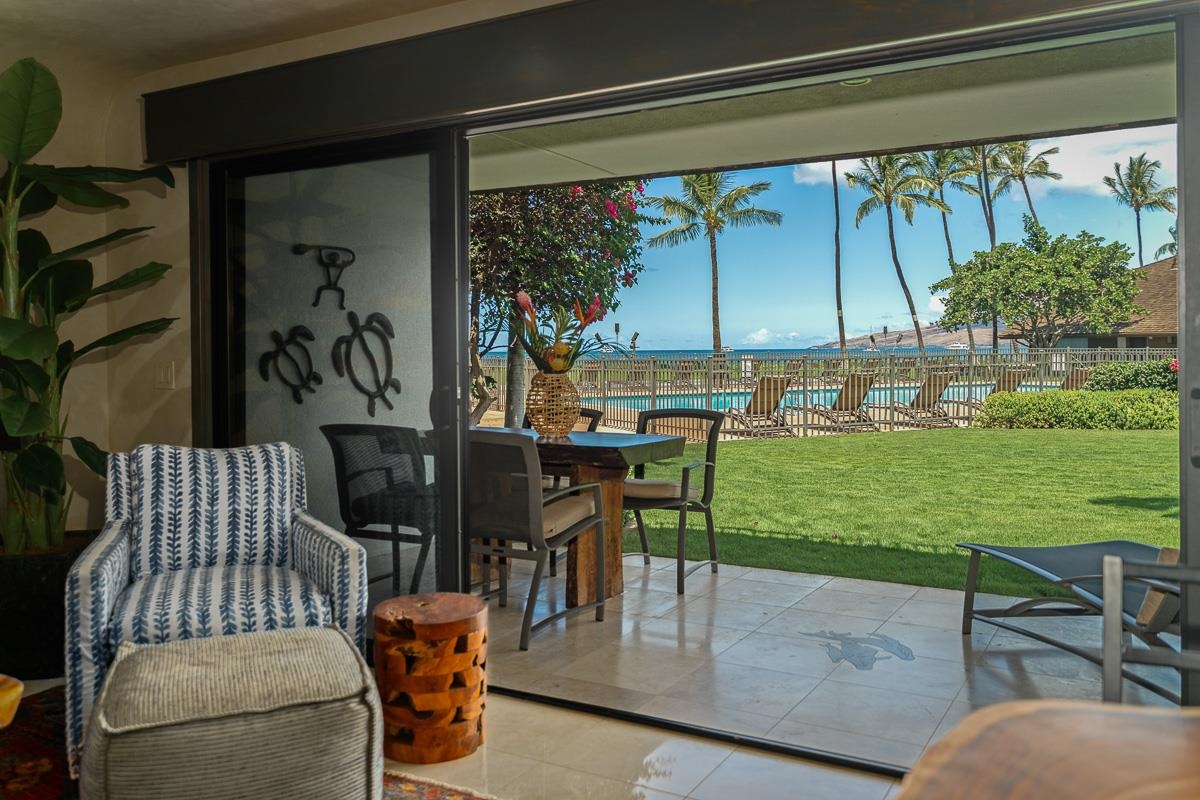 Furnished lanai opens onto a lawn, pool, palm trees, and ocean view.