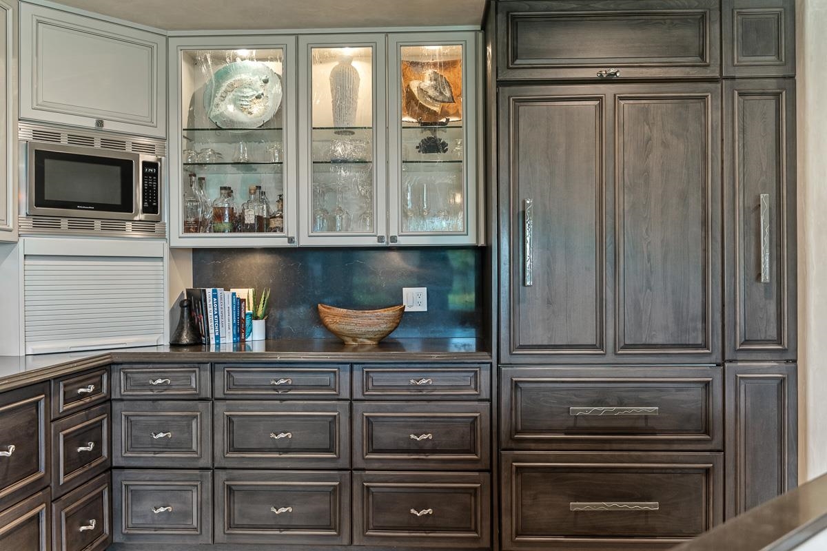 Kitchen with dark wood cabinetry, glass-front display cabinets, a built-in microwave, and a counter with a wooden bowl.