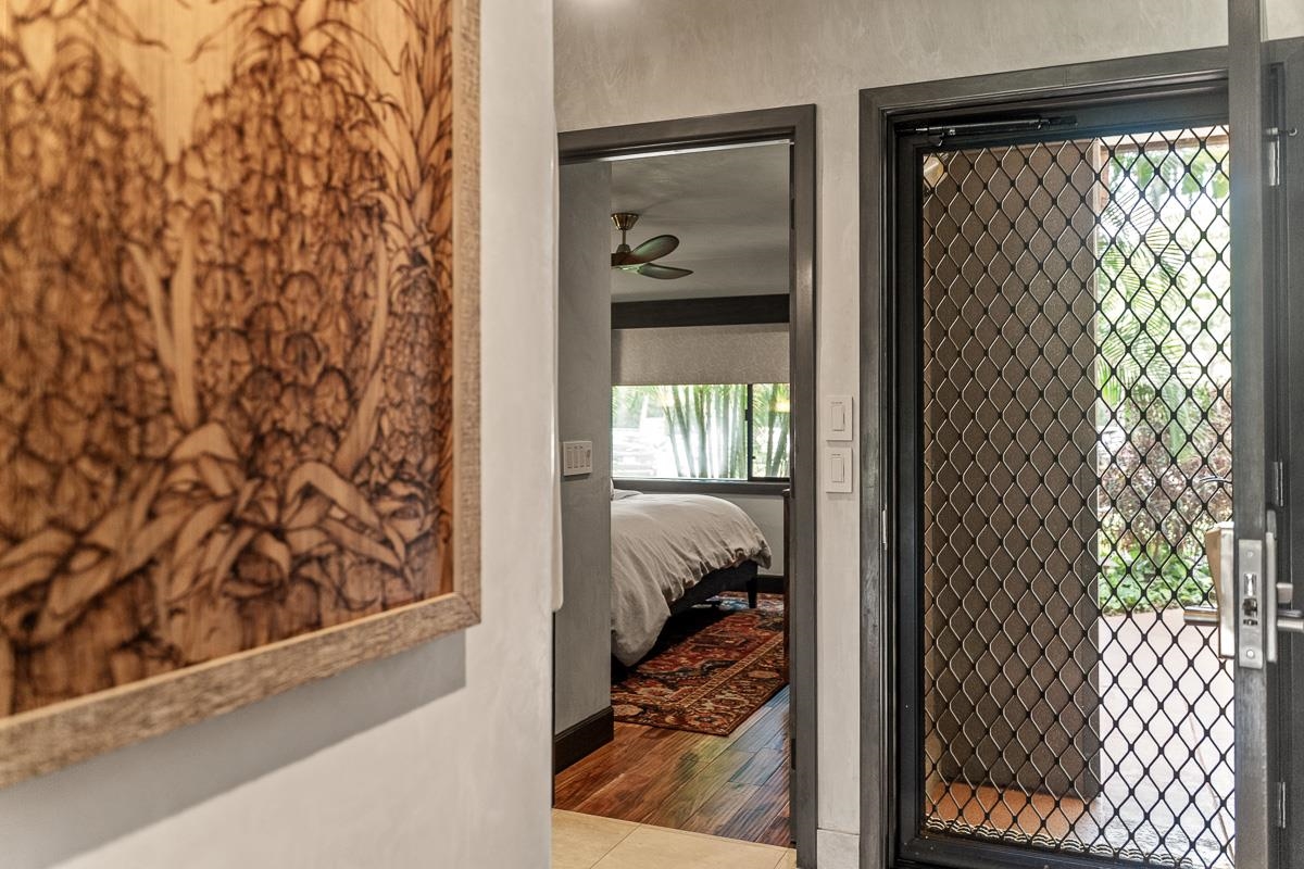 Entry hallway with framed artwork, a view into the bedroom, and a screened exterior door.