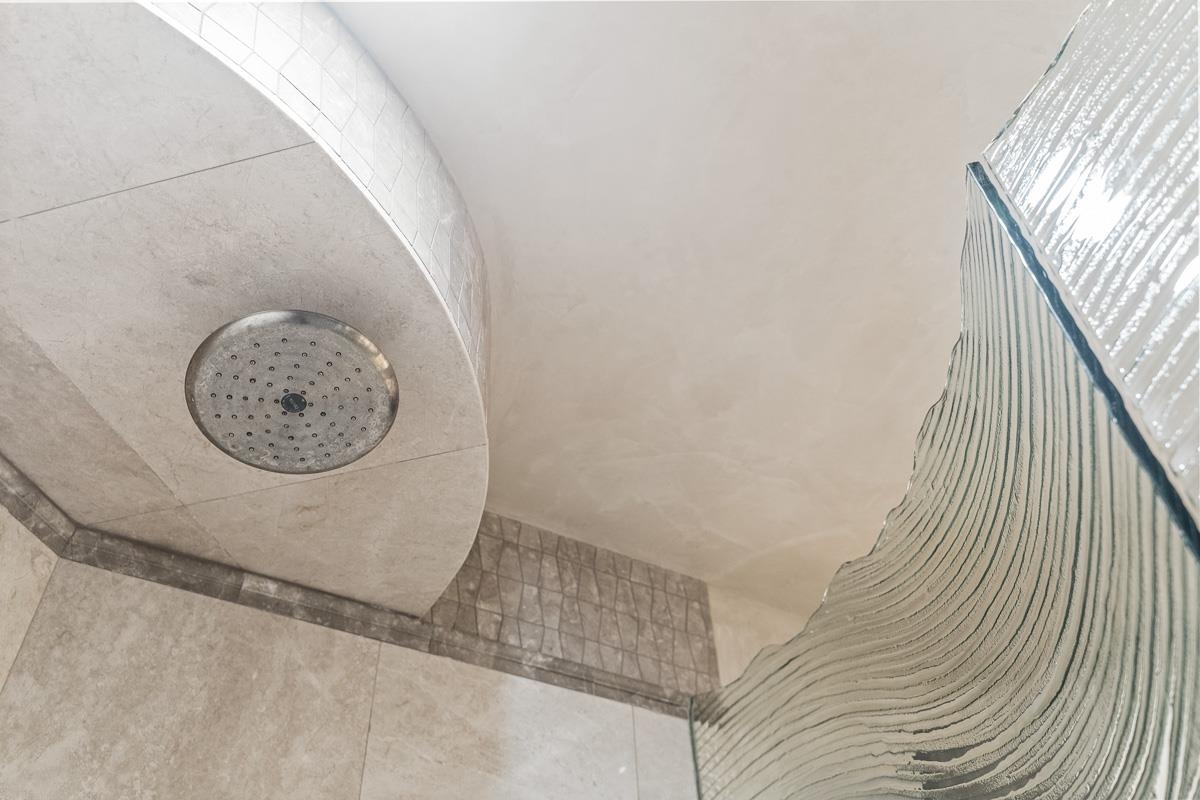 Tiled shower with a round overhead showerhead and textured glass partition.