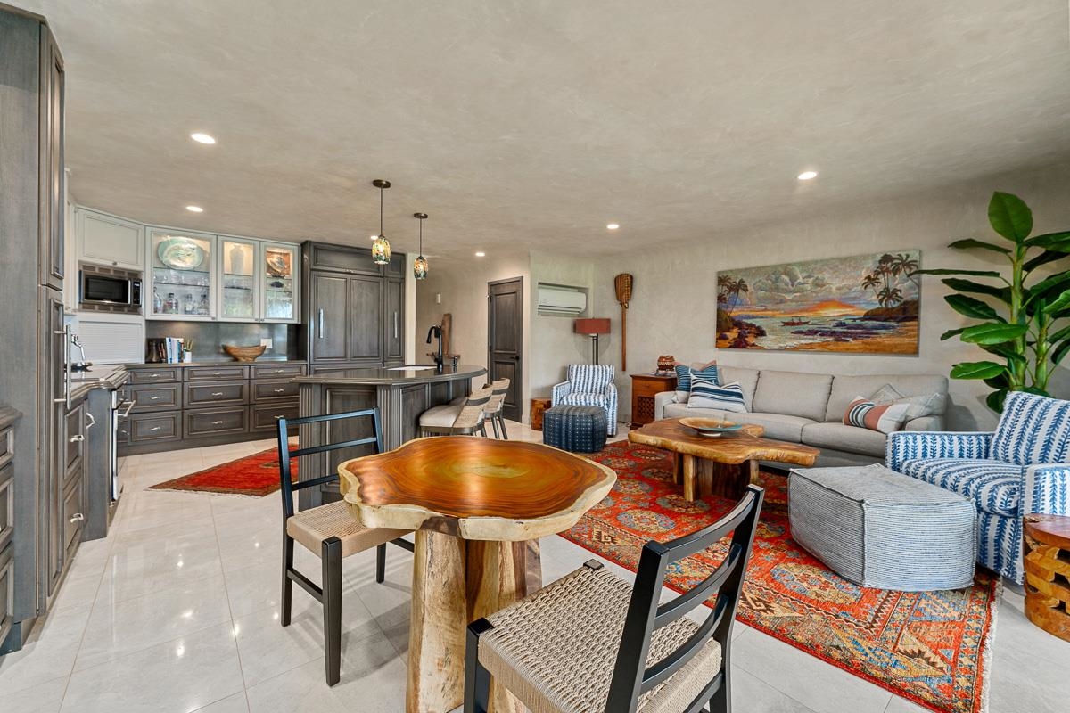 Open-plan living area with gray kitchen cabinetry, a live-edge dining table, and a colorful patterned rug.