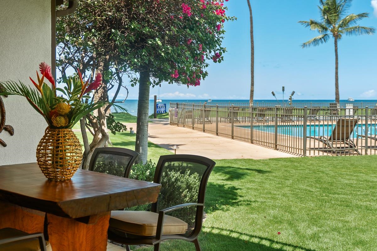Outdoor patio with a wooden dining set overlooking a swimming pool and the ocean.