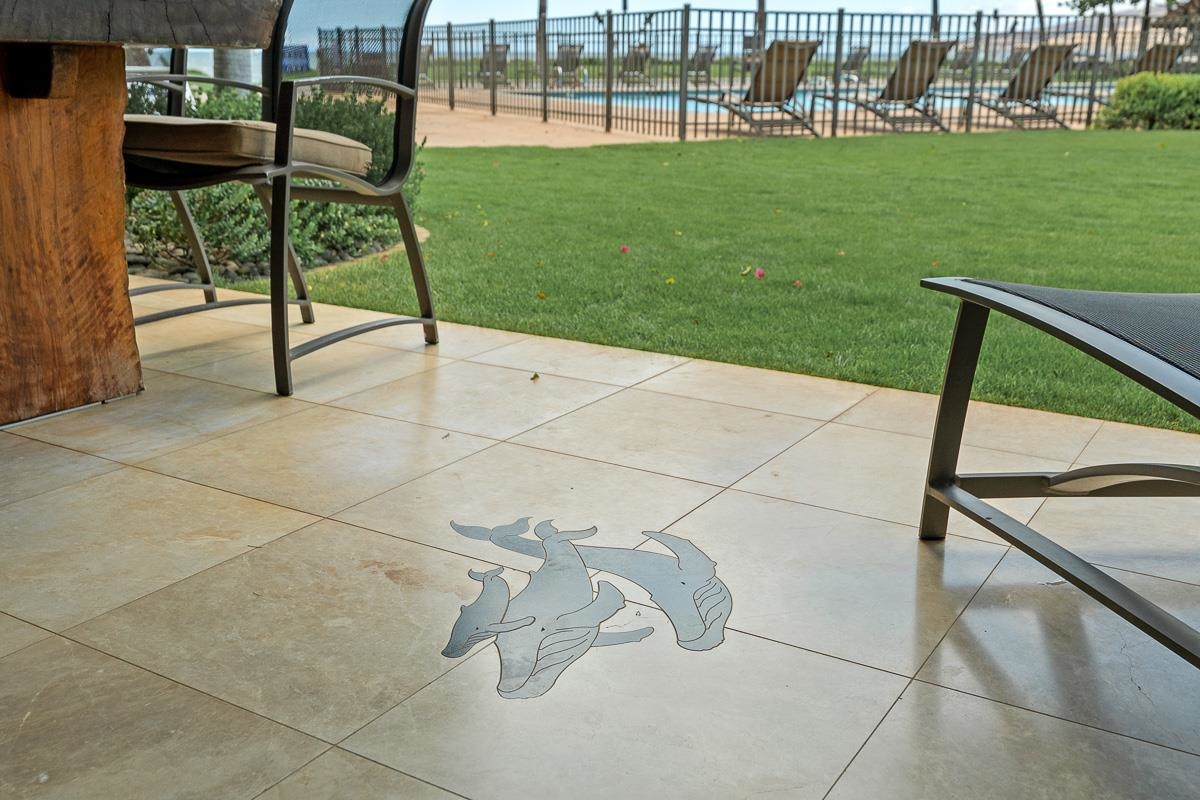 Tiled patio with a dolphin inlay overlooks a lawn and fenced swimming pool.