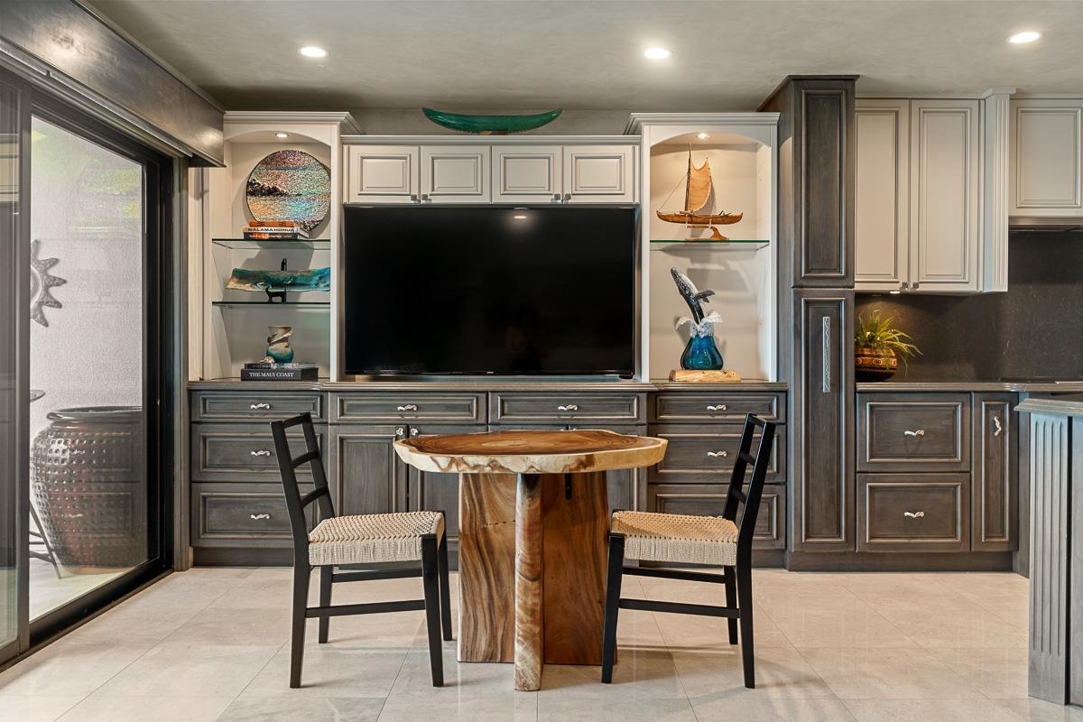 Dining area with a round wood table, two chairs, built-in cabinets, and a large television.
