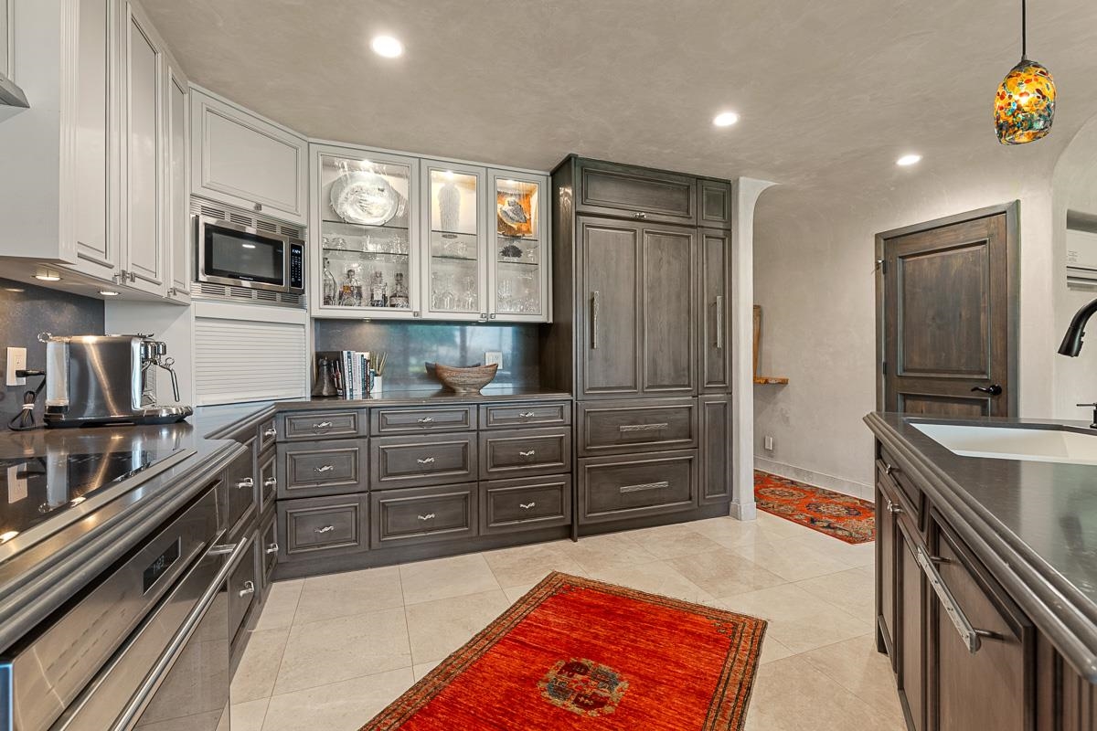 Kitchen with paneled cabinetry, glass-front cabinets, stainless appliances, and red patterned rugs.