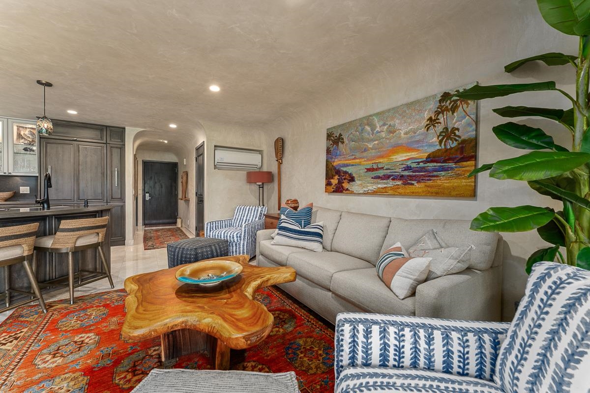 Living room with a gray sectional, patterned chairs, colorful rug, and live-edge coffee table beside the kitchen.