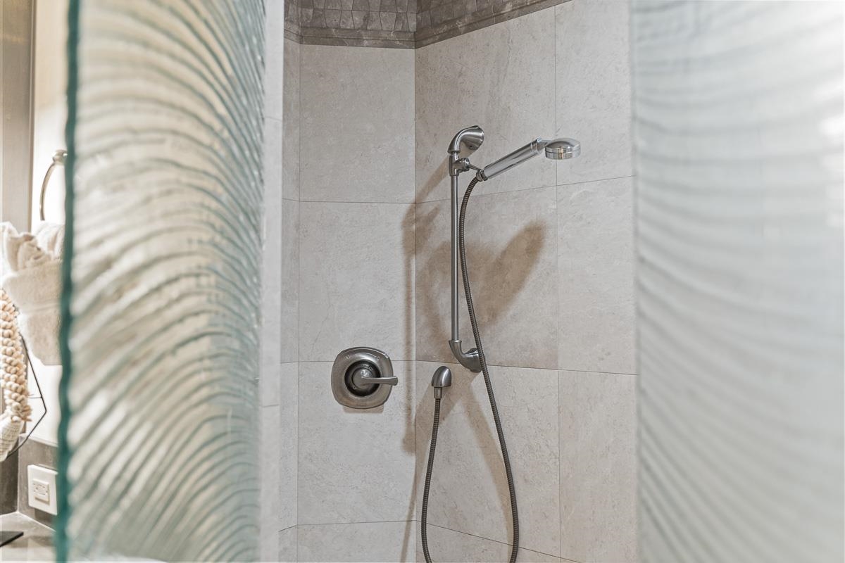 Tiled shower with chrome handheld showerhead behind patterned glass.