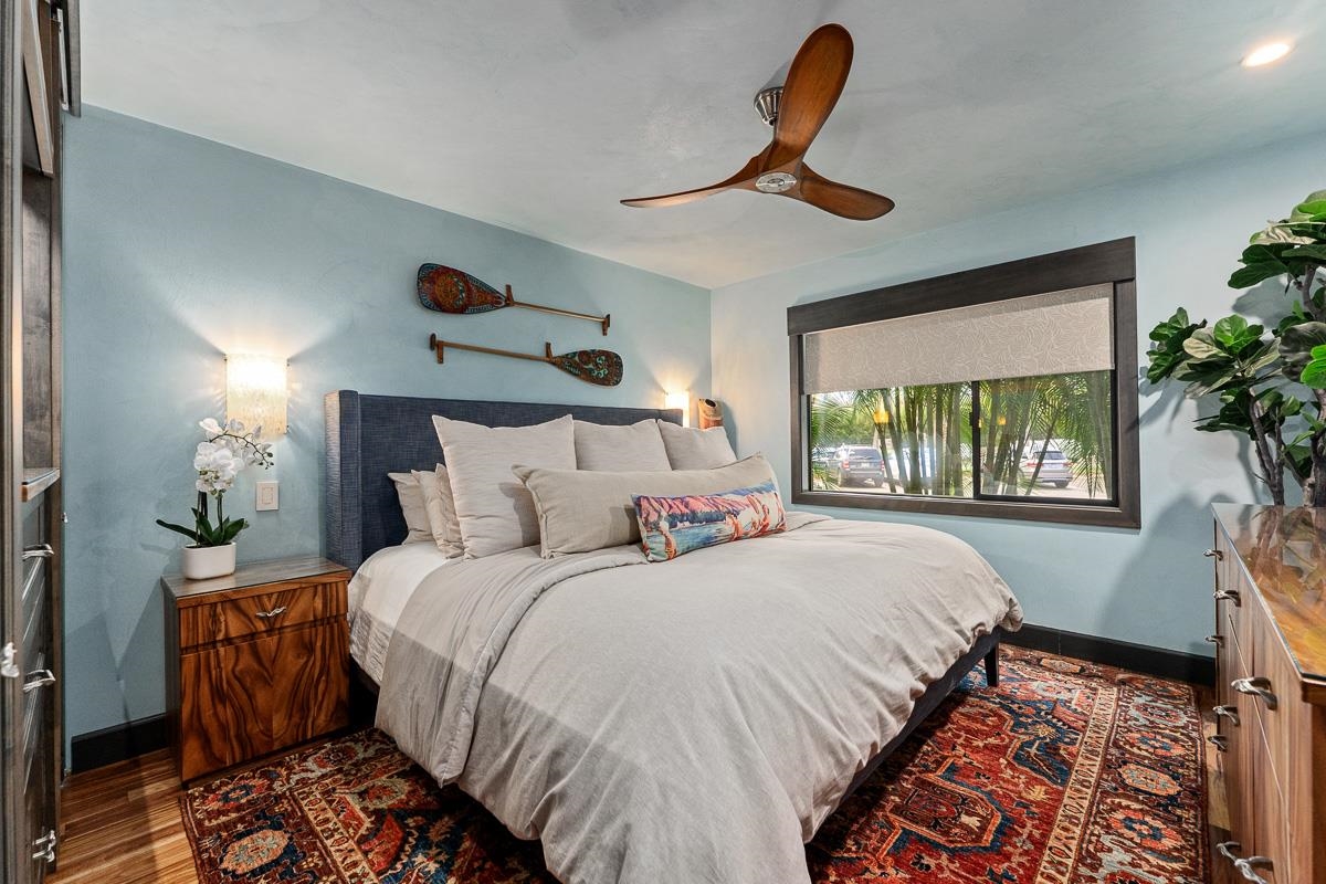 Bedroom with a large white bed, pale blue walls, and a window overlooking palm trees.