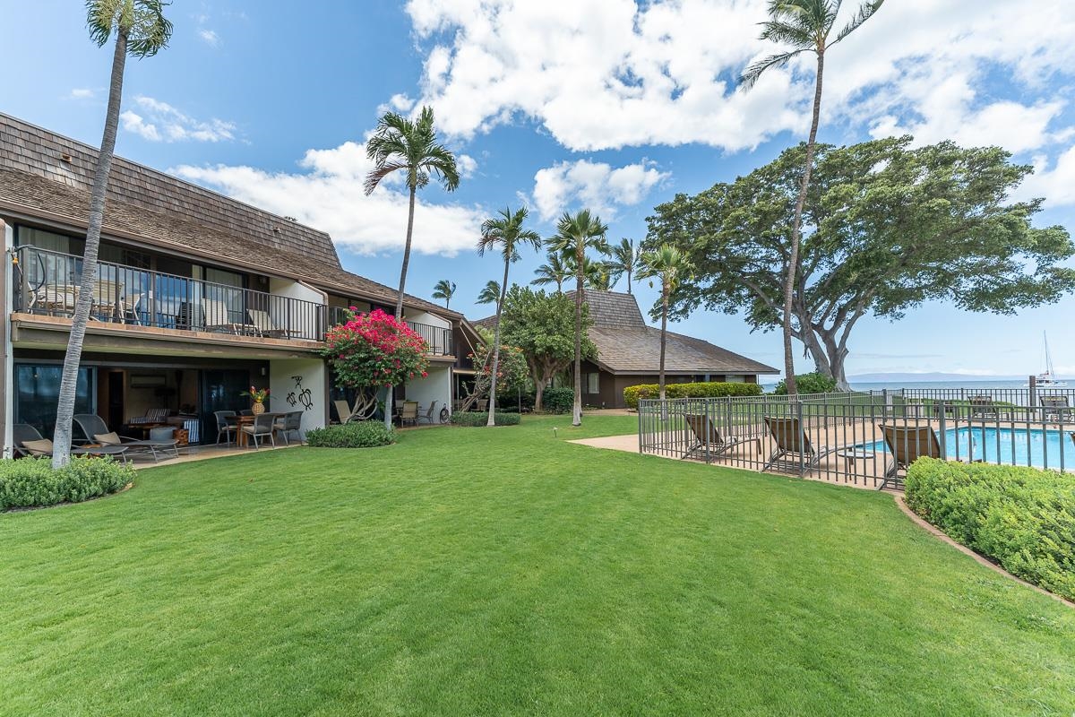 Kihei condominium grounds with a pool, palm trees, manicured lawn, and ocean view.