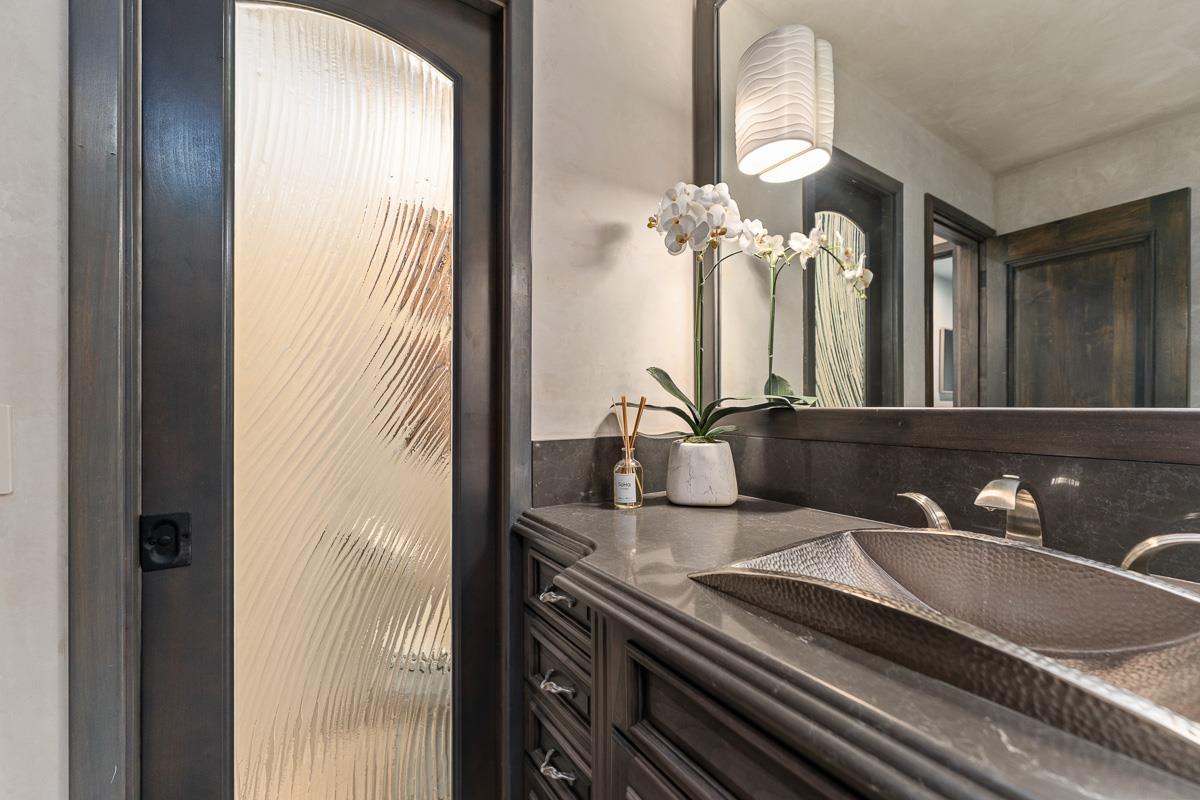 Bathroom vanity with a hammered-metal vessel sink, dark cabinetry, and white orchids.
