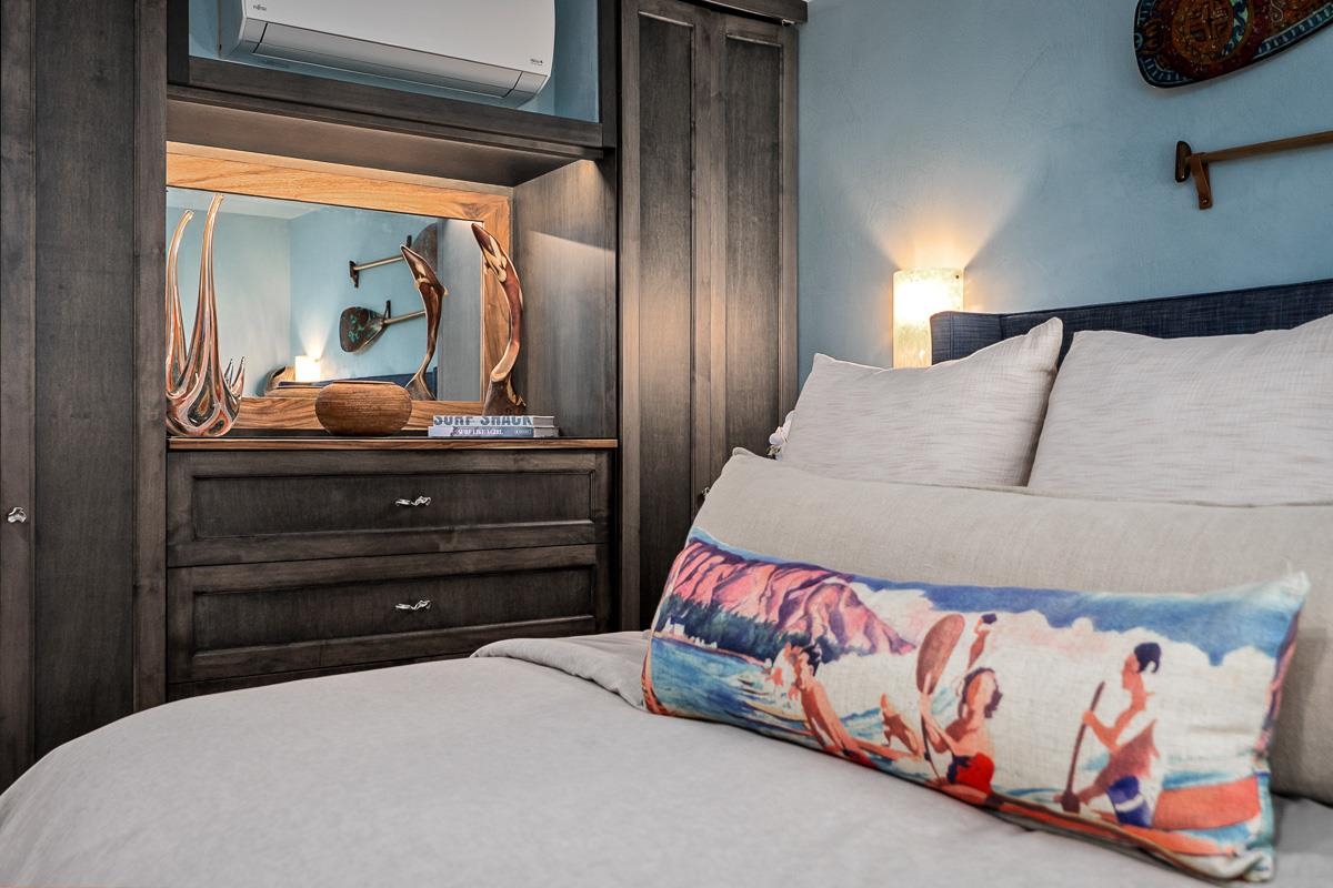 Bedroom with white bedding, a colorful surf-print pillow, and dark wood built-in cabinetry.