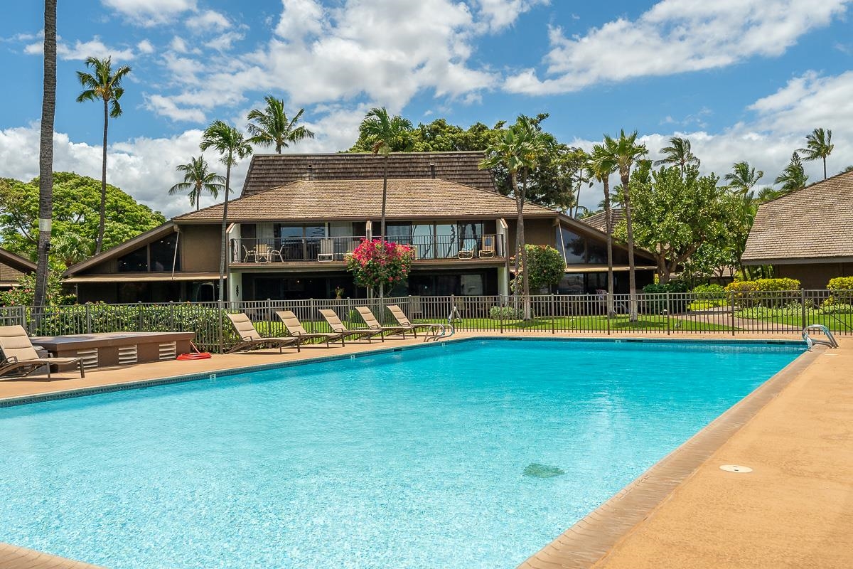 Swimming pool and lounge chairs in front of a two-story condominium building.