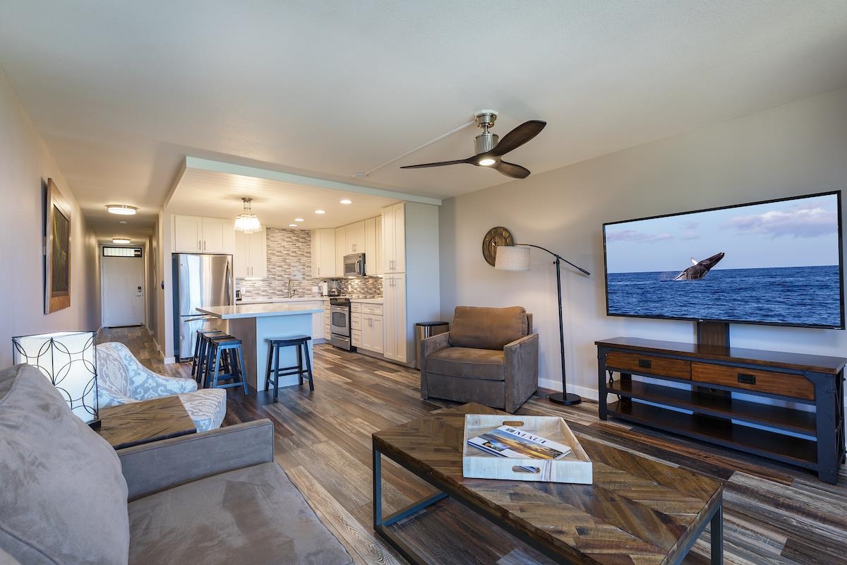 Open-plan condo living room and kitchen with a breakfast bar, stainless appliances, and gray seating.